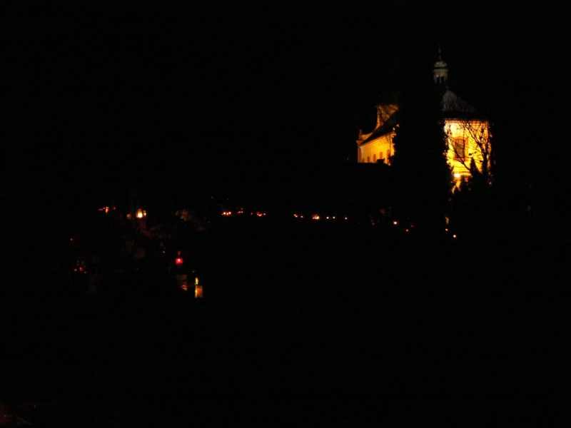 Světýlka, planoucí na hrobech a klášterní kostel v pozadí.